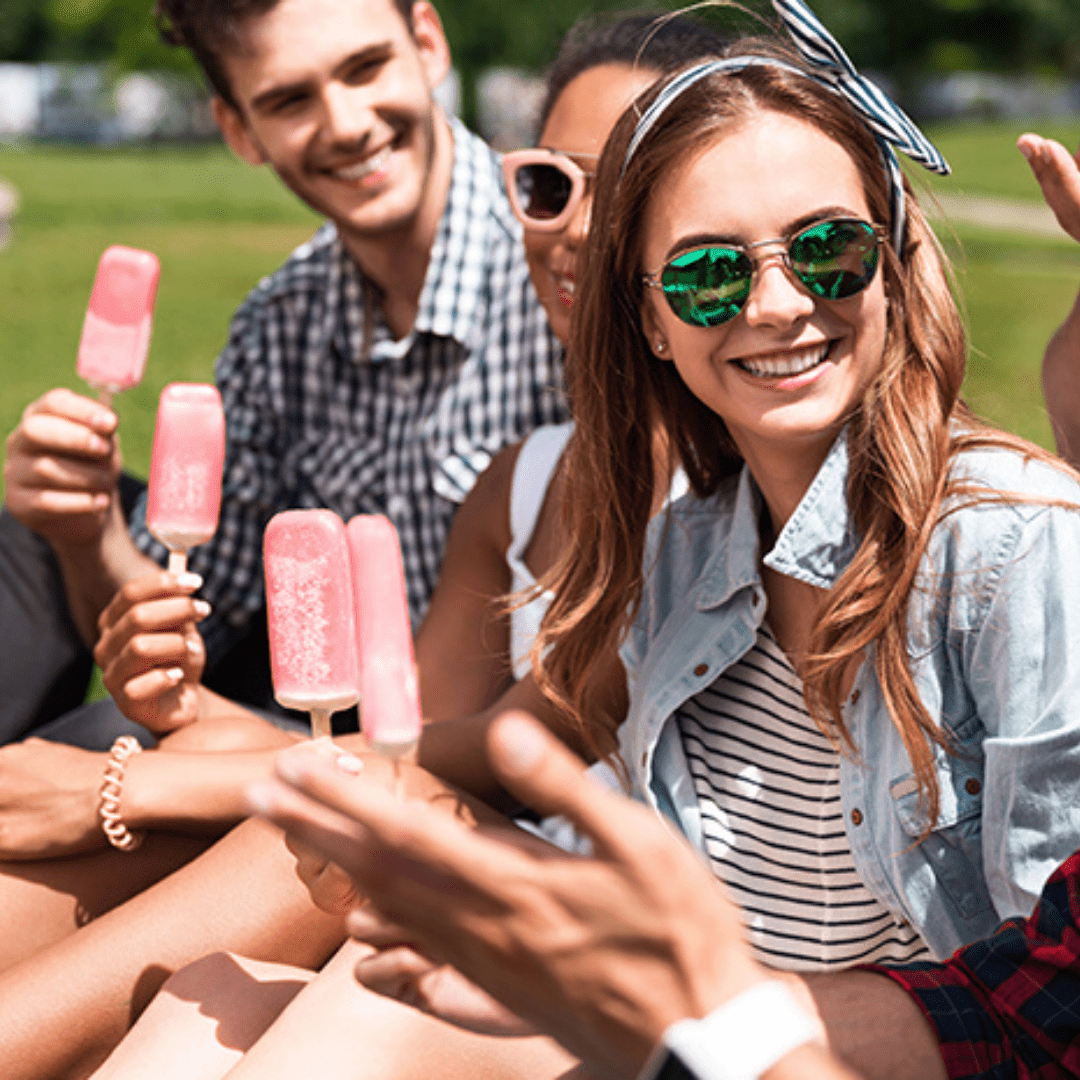 A group of people sitting around each other holding popsicles.