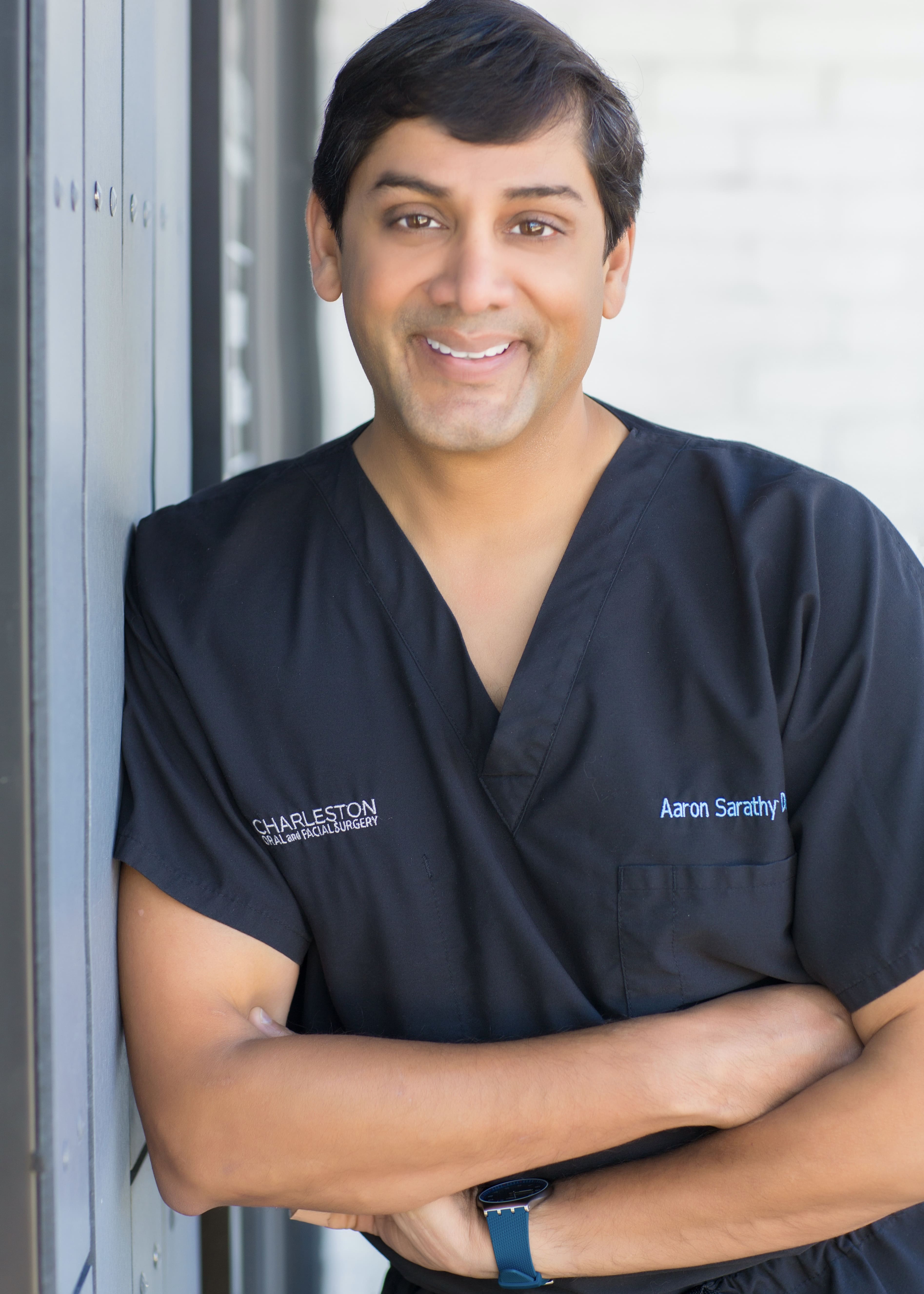 A man in black scrubs standing next to a wall.