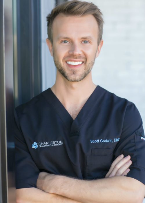 A man in black scrubs standing next to a window.