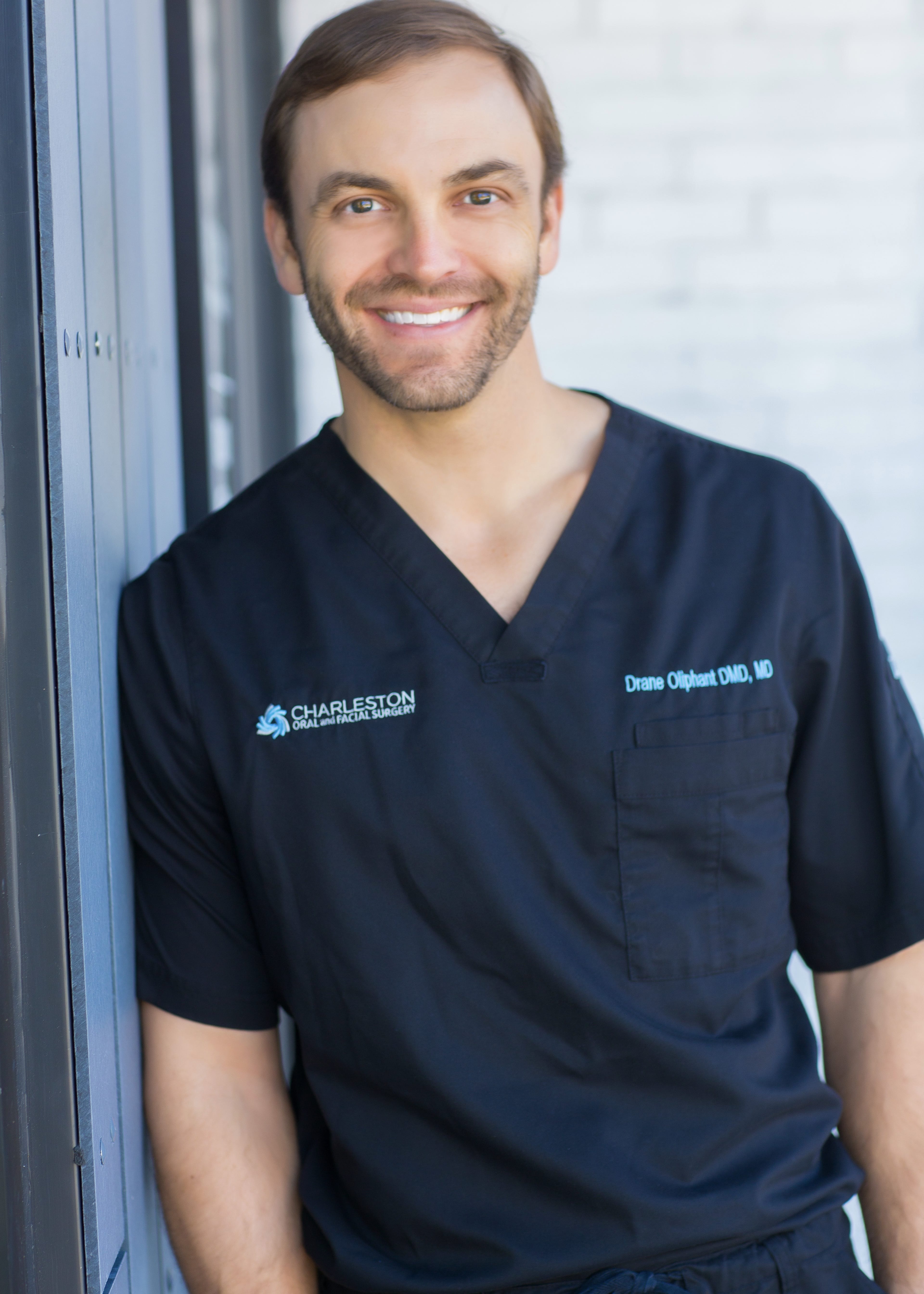 A man in black scrubs standing next to a window.