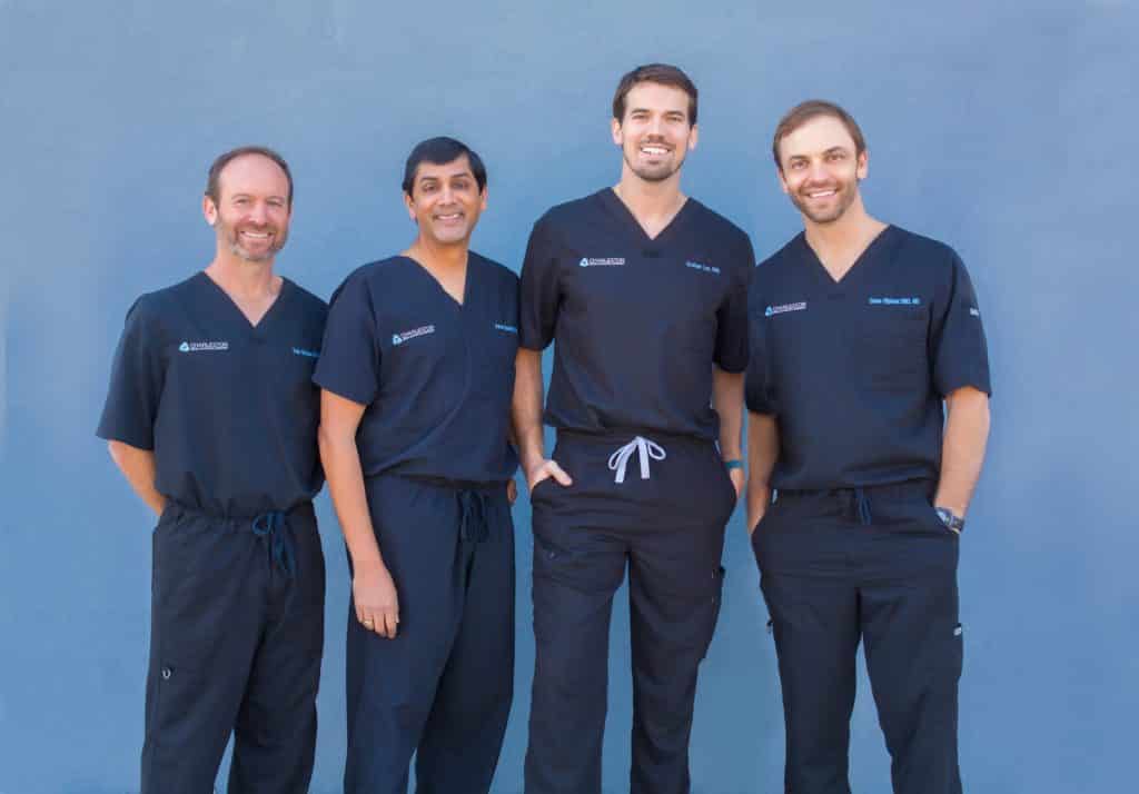 Four doctors standing in front of a blue wall.