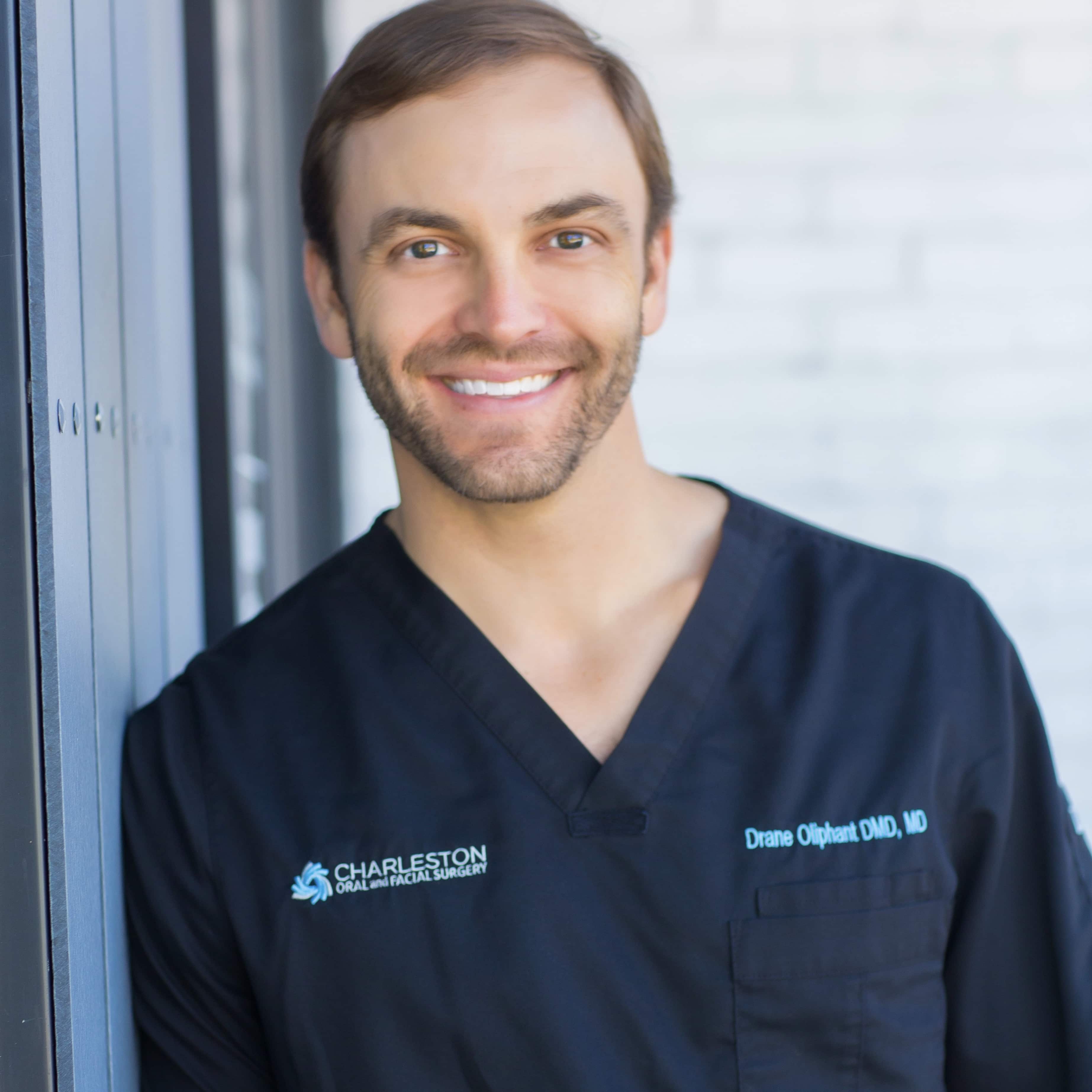 A man in black scrubs standing next to a window.