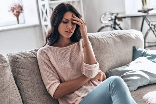 A woman sitting on top of the couch holding her head.